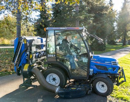 Angestellter im technischen Dienst. Der Mitarbeiter sitzt auf einerm kleinen Rasenmähertraktor. Im Hintergrund eine Parkansicht.