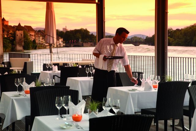 Kellner deckt Tische auf Rheinterrasse bei Abendstimmung